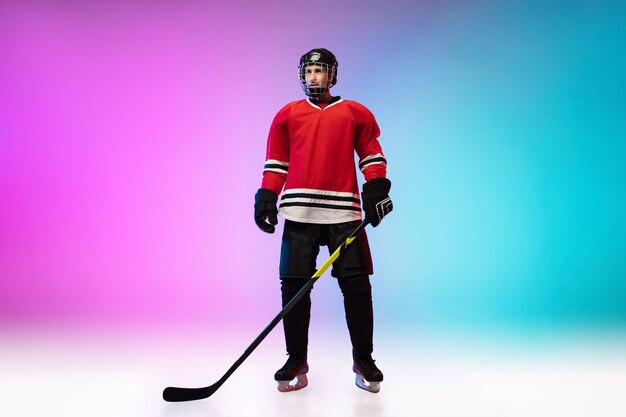 Male hockey player with the stick posing on ice court and neon colored gradient wall