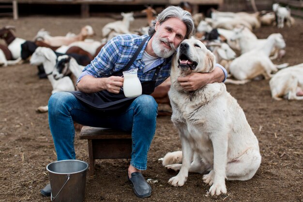 Male holding cup of goat milk while playing with dog