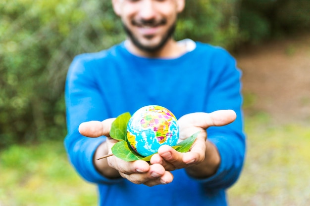 Бесплатное фото Мужчина держит глобус с зеленым листом и улыбается