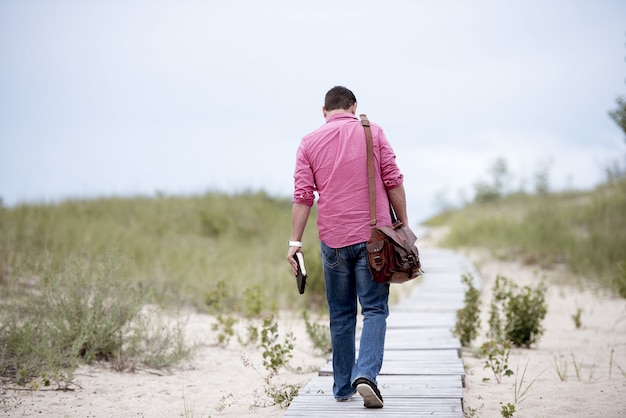 Male holding a notebook walking on a wooden pathway in the middle of sandy surface