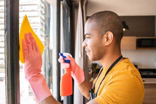 Male housekeeper cleaning glass window at home.