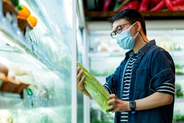 フェイスマスク保護の手を身に着けている男性の夫は、食料品店のスーパーマーケットでのvagetableショッピングを選択します新しい通常のライフスタイルの健康とアイデアのコンセプト