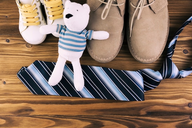 Male and kid boots near tie with soft toy