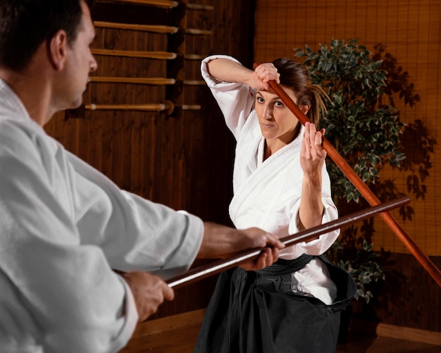 Male martial arts instructor in the practice hall with wooden stick and female trainee