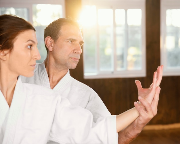 Male martial arts instructor training with female trainee in practice hall with copy space