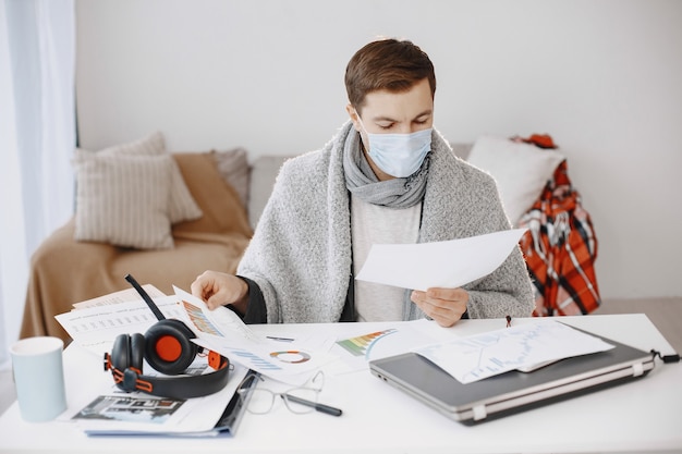 Maschio in una maschera medica. uomo seduto nel soggiorno di casa. ragazzo che si diverte a studiare in quarantena.