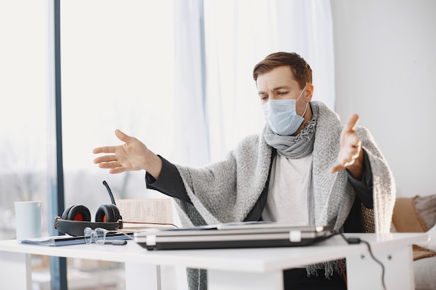 Maschio in una maschera medica. uomo seduto nel soggiorno di casa. ragazzo che si diverte a studiare in quarantena.