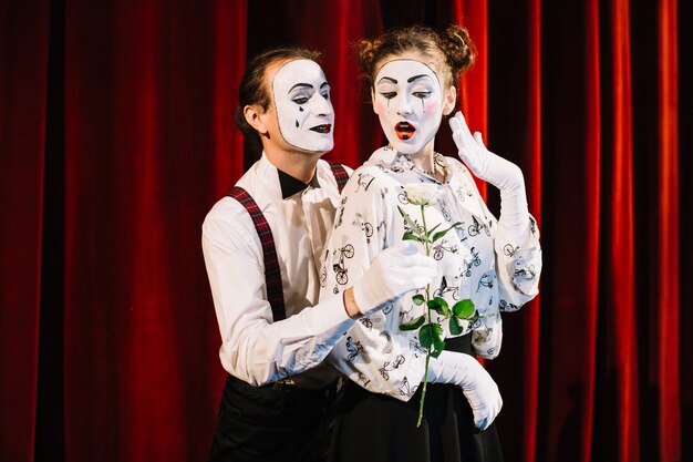 Male mime artist giving white rose to female mime