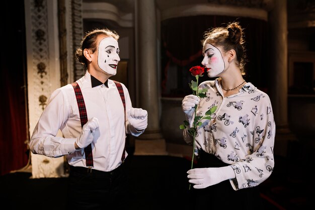 Male mime artist looking at female mime smelling red rose