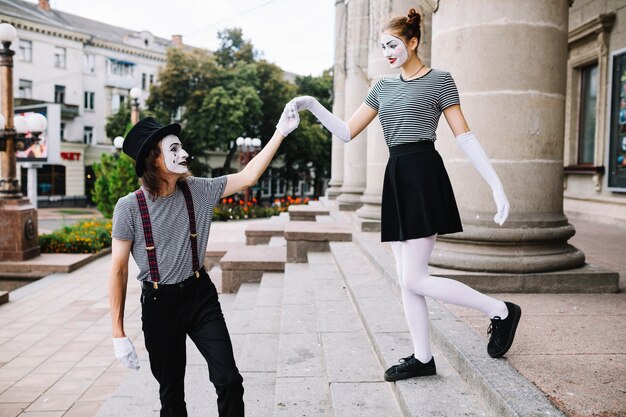 Male mime assisting female mime climbing down staircase