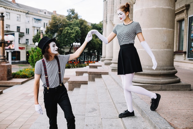 Male mime assisting female mime climbing down staircase