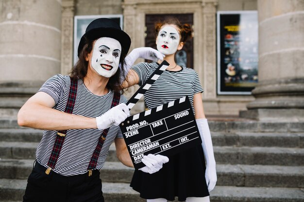 思慮深い女性のmimeの前にclapperboardを保持している男性のmime