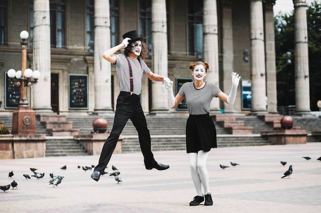 Male mime holding female mime's hand jumping in front of building
