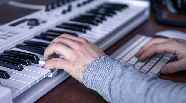 男性ミュージシャンは、コンピューターとキーボードのミュージシャンの職場を使用して音楽を作成します