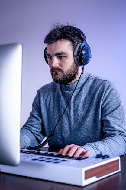 男性ミュージシャンは、コンピューターとキーボードのミュージシャンの職場を使用して音楽を作成します