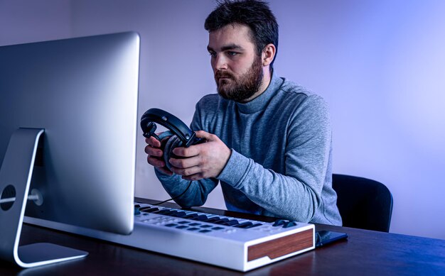 男性ミュージシャンは、コンピューターとキーボードのミュージシャンの職場を使用して音楽を作成します