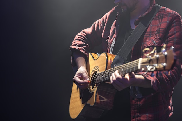 Бесплатное фото Мужской музыкант, играющий на акустической гитаре в копировальном пространстве темной комнаты.