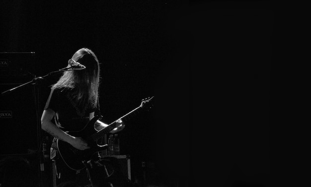 Мужской музыкант играет на гитаре на сцене возле микрофона в черно-белом