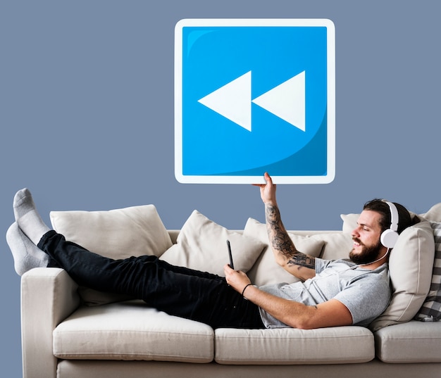 Бесплатное фото Мужчина на диване, удерживая значок кнопки перемотки
