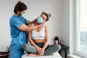 Foto gratuita terapista osteopatico maschio con mascherina medica che controlla i muscoli del collo del paziente femminile
