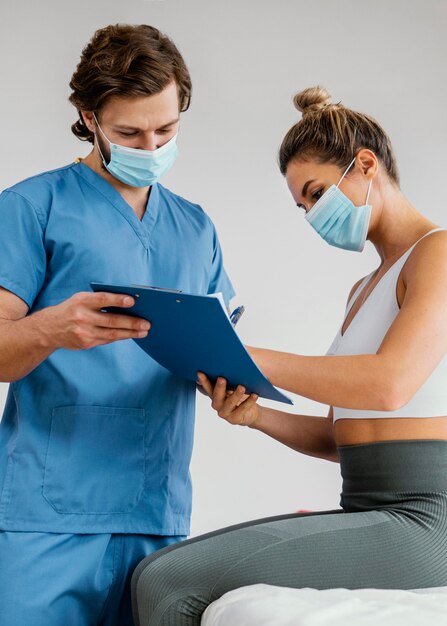 male osteopathic therapist with medical mask and female patient in the office signing clipboard