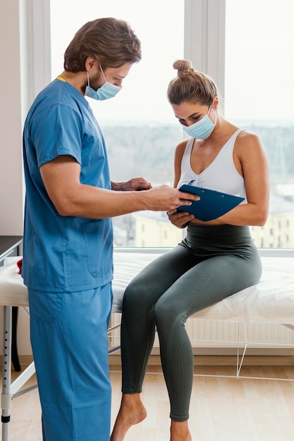 Male osteopathic therapist with medical mask and patient in the office signing clipboard
