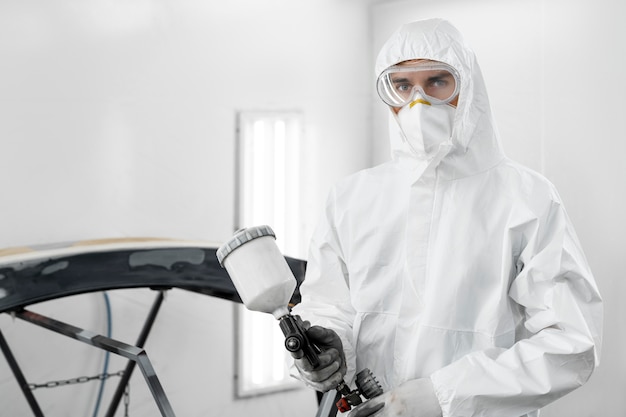 Male painter using gun to paint car in the shop