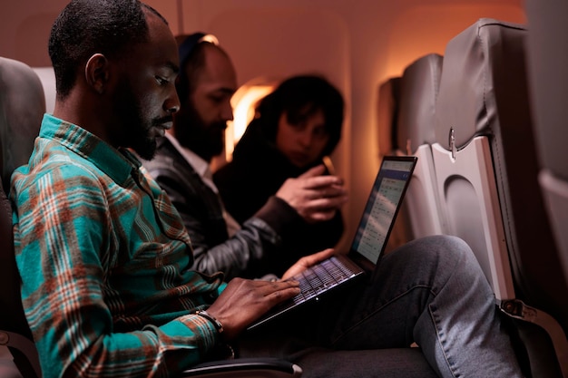 항공 서비스와 항공 운송을 이용하여 국제선 비행기로 해외 여행을 하는 남성 승객. 이코노미 클래스에서 일몰 동안 노트북 컴퓨터를 사용하는 프리랜서.