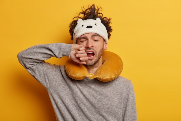 Male passenger wearing inflated travel pillow over neck and cute eye mask