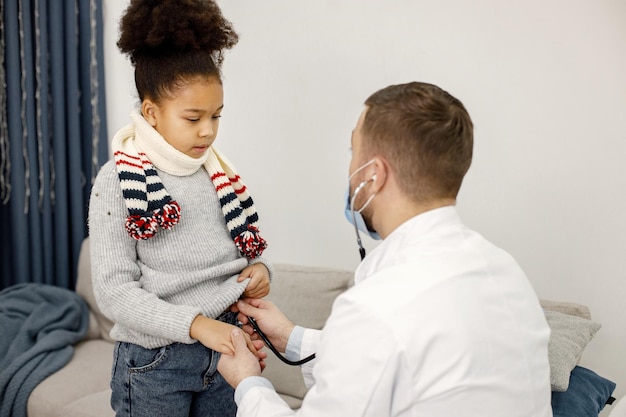 stethoskope와 아픈 작은 흑인 소녀를 검사하는 남성 소아과 의사