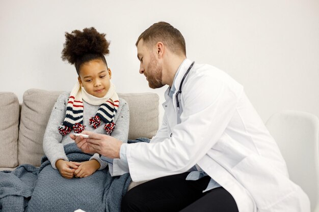 病気の小さな黒い女の子を調べる男性の小児科医