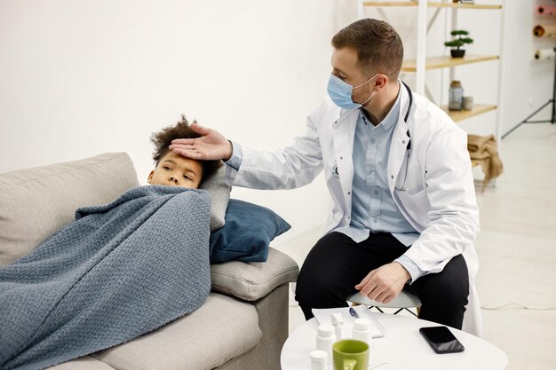 Male pediatrician holding hand on a forehead of sick little black girl