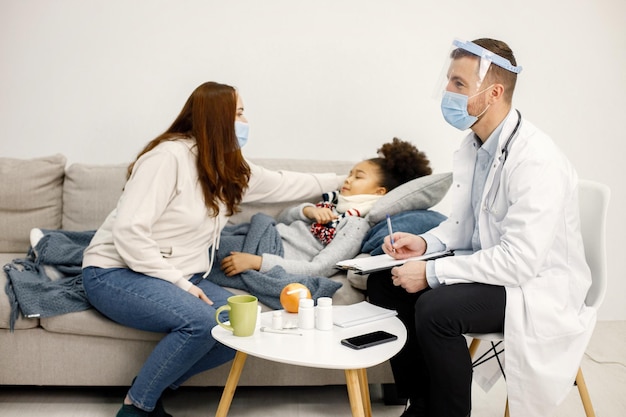 Male pediatrician talking with mother of sick little black girl