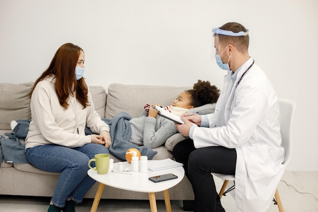 Male pediatrician talking with mother of sick little black girl