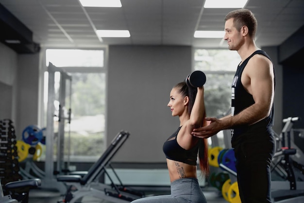 Male personal trainer helping woman working with heavy dumbbells at gym