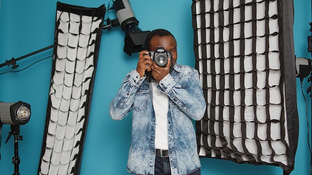 Free photo male photographer using dslr camera and lens to take pictures in studio backstage, capturing photos with professional equipment. using focused view to photograph images over background.