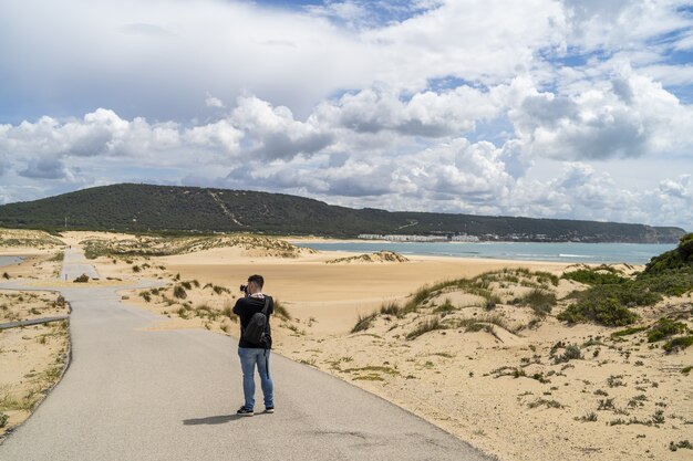 スペイン、アンダルシアの日中に曇り空の下でビーチを歩く男性写真家