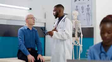 Free photo male physician showing radiography scan to sick patient, explaining bones diagnosis at medical appointment. general practitioner and old man analyzing x ray test results to find treatment.