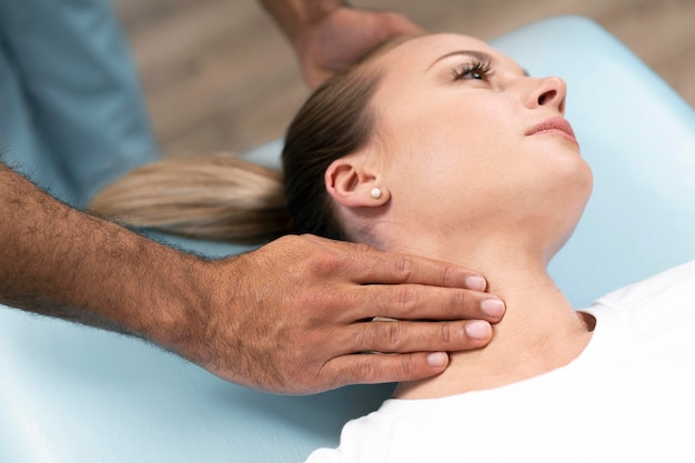 Male physiotherapist checking woman's neck while sitting on bed