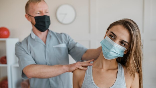 女性患者との治療セッション中に医療用マスクを着用している男性の理学療法士