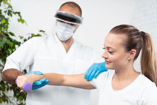 Male physiotherapist with face shield checking woman's arm