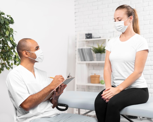 Male physiotherapist with medical mask checking woman
