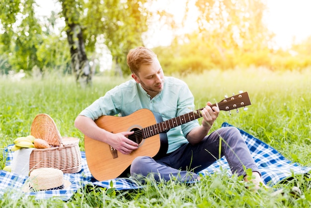 男性の夏にピクニックにギターを弾く
