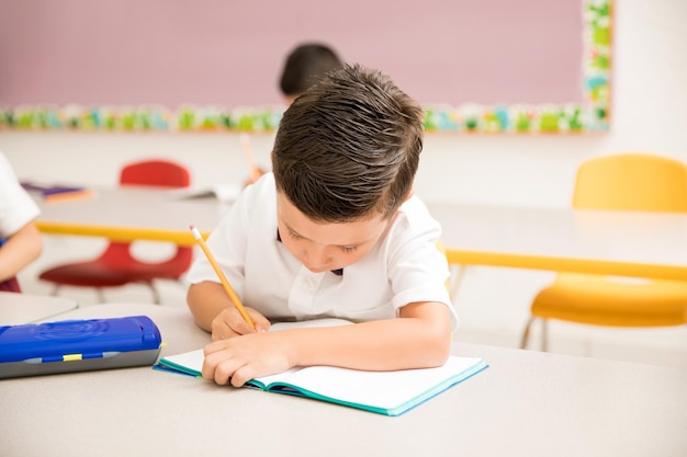 Male preschooler wearing uniform and working on a writing assigment in the classroom