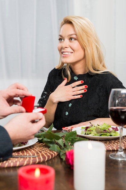 Male presenting gift box with ring to surprised female at table