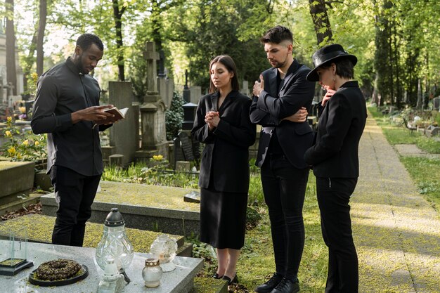 Male priest reading from the bible at the grave with mourning family