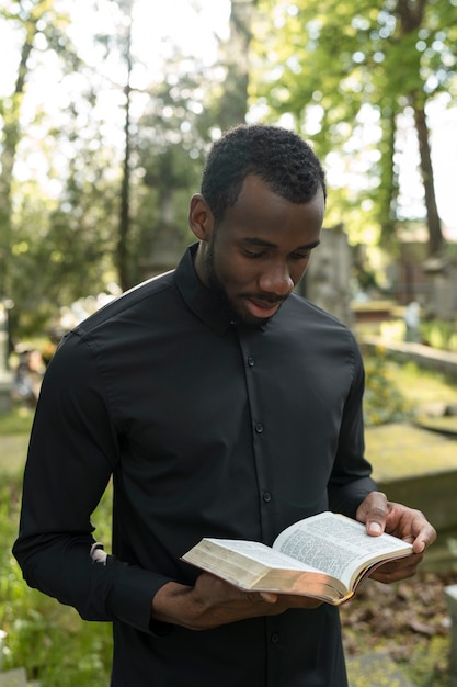 Male priest reading from the bible at the grave with mourning family