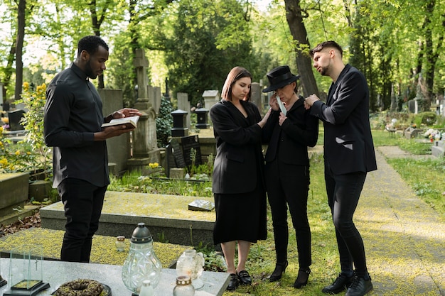 Male priest reading from the bible at the grave with mourning family