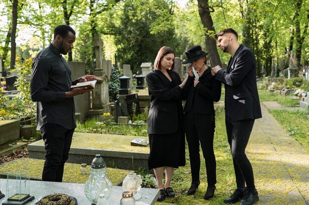 male priest reading from the bible at the grave with mourning family