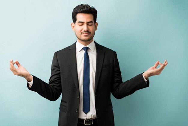 Male professional in suit gesturing while meditating against blue background
